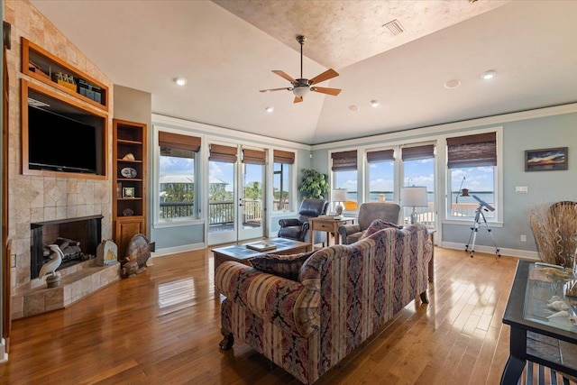 living room featuring built in shelves, ceiling fan, wood-type flooring, lofted ceiling, and a tiled fireplace