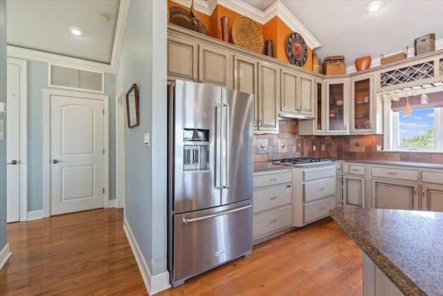 kitchen featuring backsplash, ornamental molding, appliances with stainless steel finishes, cream cabinetry, and light hardwood / wood-style floors