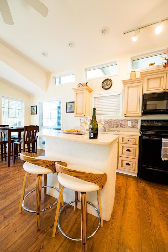 kitchen featuring dark wood-type flooring, black appliances, ceiling fan, a breakfast bar, and backsplash