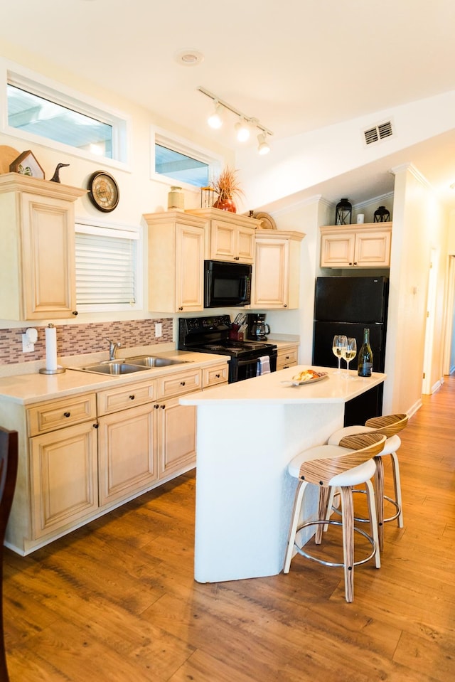 kitchen with a kitchen bar, light wood-type flooring, black appliances, and tasteful backsplash