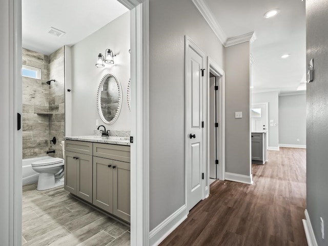 full bathroom with ornamental molding, vanity, hardwood / wood-style floors, toilet, and tiled shower / bath