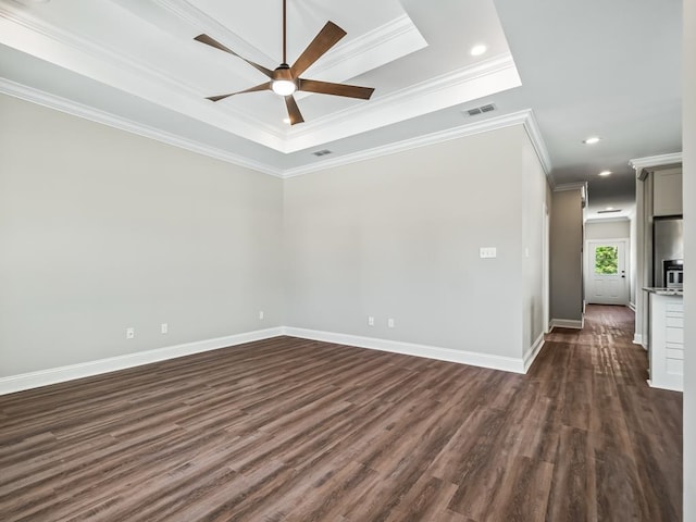 empty room featuring a raised ceiling, dark wood-type flooring, ceiling fan, and crown molding