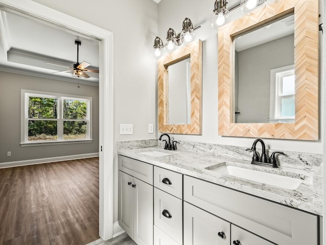 bathroom with wood-type flooring, crown molding, vanity, a tray ceiling, and ceiling fan