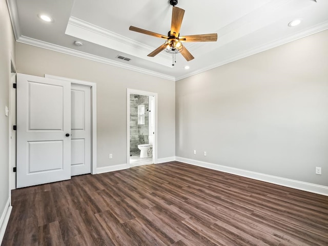 unfurnished bedroom featuring crown molding, connected bathroom, dark hardwood / wood-style flooring, a tray ceiling, and ceiling fan