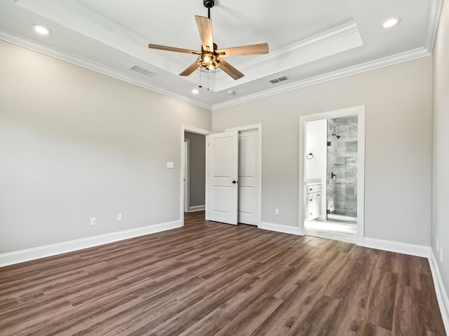 unfurnished bedroom featuring crown molding, ensuite bath, dark wood-type flooring, a tray ceiling, and ceiling fan