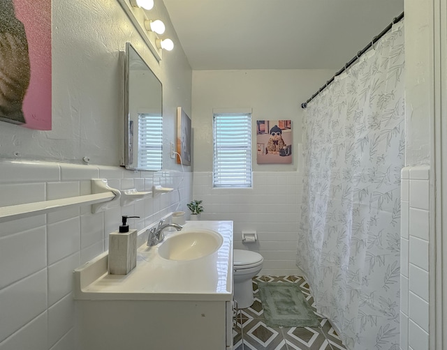 bathroom with toilet, a wainscoted wall, a shower with shower curtain, vanity, and tile walls