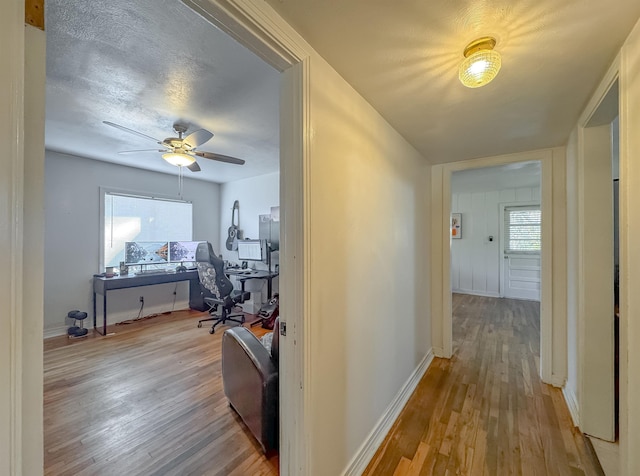 hallway with light wood-style floors, baseboards, and a textured ceiling