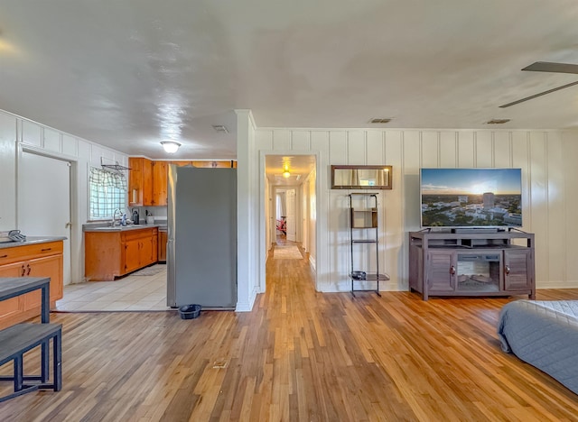 kitchen featuring brown cabinetry, freestanding refrigerator, light countertops, light wood-style floors, and a sink