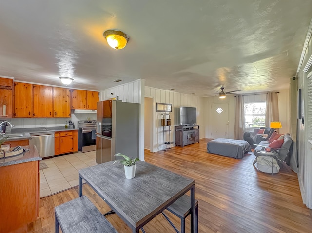 kitchen with brown cabinets, open floor plan, stainless steel appliances, light countertops, and light wood-style floors