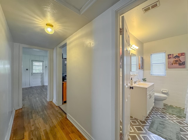 hall with light wood-style floors, visible vents, a sink, and tile walls