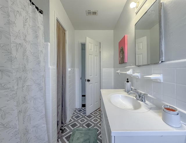 full bath featuring curtained shower, vanity, visible vents, tile walls, and wainscoting