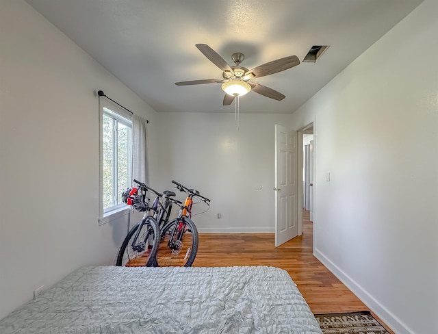 bedroom with light wood finished floors, ceiling fan, visible vents, and baseboards