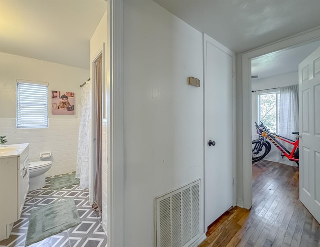 corridor featuring light wood-style floors, wainscoting, visible vents, and tile walls