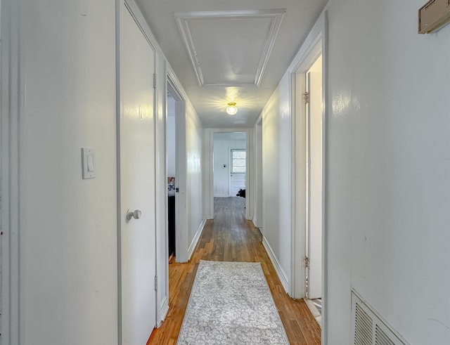 hall with attic access, visible vents, light wood-style floors, and baseboards