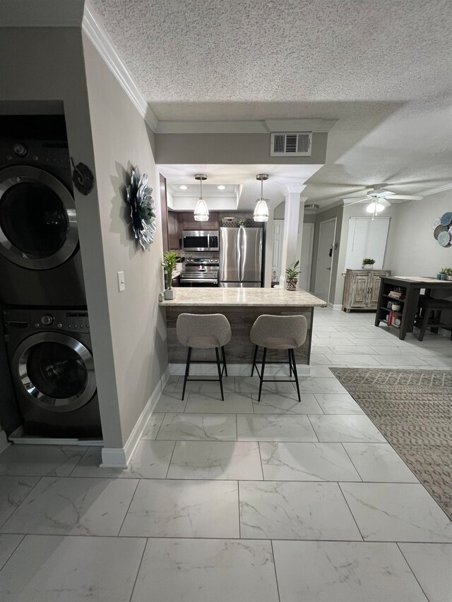 kitchen with appliances with stainless steel finishes, a textured ceiling, hanging light fixtures, stacked washer / drying machine, and kitchen peninsula