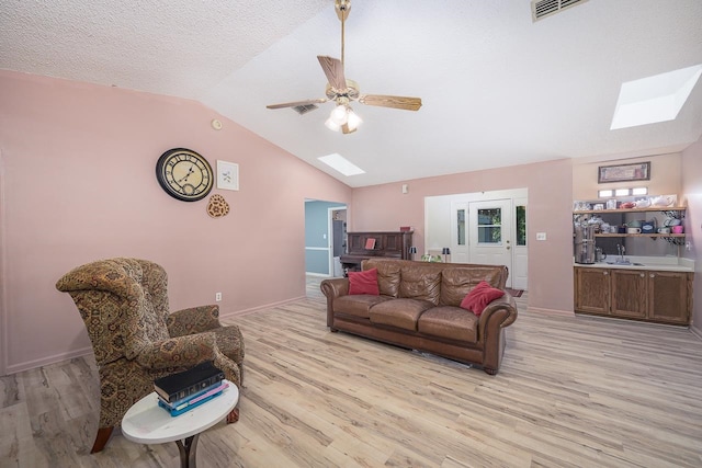 living room featuring ceiling fan, vaulted ceiling with skylight, sink, and light wood-type flooring