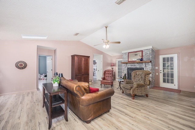 living room featuring a fireplace, light hardwood / wood-style flooring, vaulted ceiling, and ceiling fan