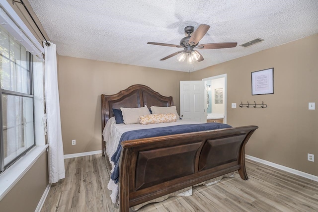 bedroom featuring a textured ceiling, ensuite bathroom, light hardwood / wood-style flooring, and ceiling fan