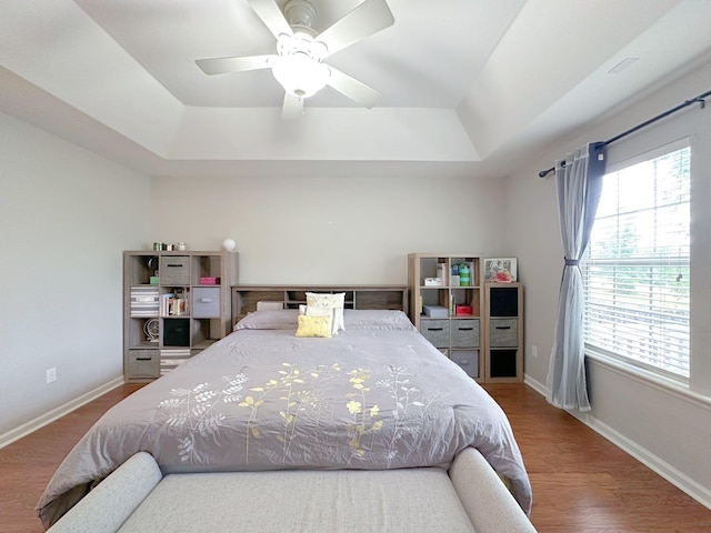 bedroom featuring a tray ceiling, wood finished floors, baseboards, and a ceiling fan