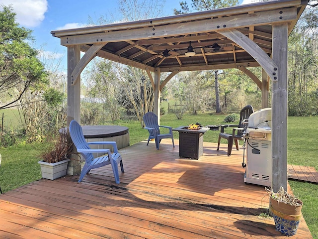 deck featuring a yard, ceiling fan, an outdoor fire pit, a hot tub, and a gazebo