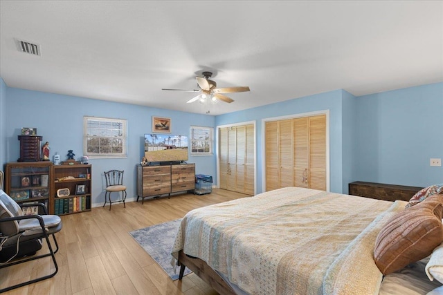 bedroom with a ceiling fan, visible vents, baseboards, light wood finished floors, and two closets