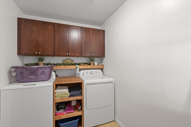 laundry room with washing machine and dryer, cabinet space, a textured ceiling, and baseboards