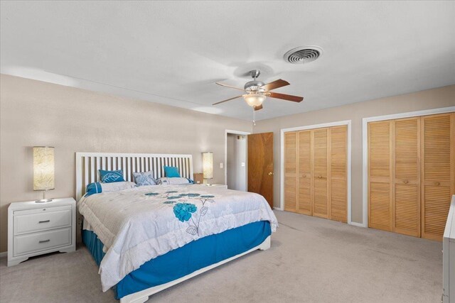 carpeted bedroom with visible vents, ceiling fan, and two closets