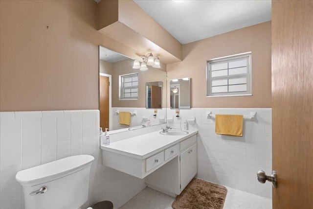 bathroom with wainscoting, toilet, tile patterned flooring, vanity, and tile walls