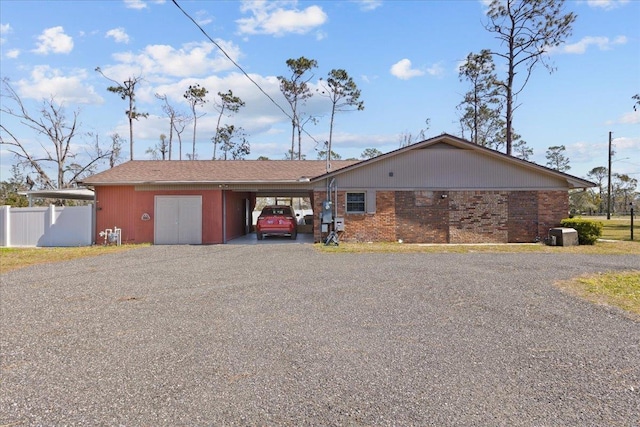 single story home featuring a carport, brick siding, gravel driveway, and fence