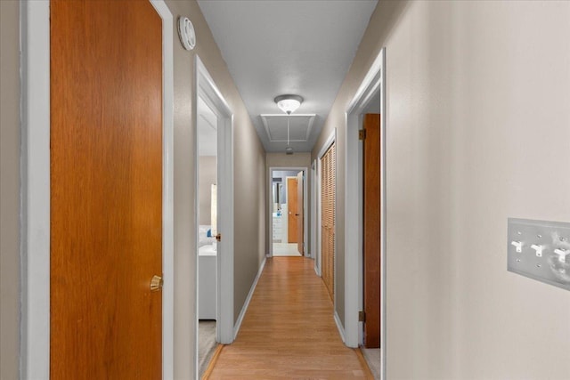 hallway featuring attic access, light wood-style flooring, and baseboards