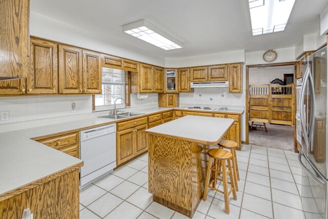 kitchen featuring sink, a breakfast bar area, light tile patterned floors, white appliances, and a center island