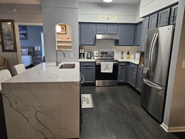 kitchen featuring gray cabinetry, stainless steel appliances, a sink, light stone countertops, and dark wood-style floors