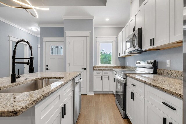 279 Ayers Ct, Tallahassee, FL 32305 - kitchen with appliances with stainless steel finishes, a sink, white cabinets, light wood-type flooring, and crown molding