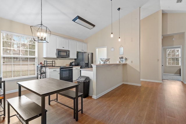 kitchen with appliances with stainless steel finishes, hanging light fixtures, white cabinets, kitchen peninsula, and light wood-type flooring