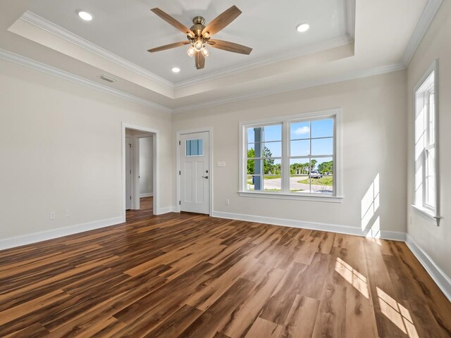 empty room featuring wood-type flooring, a healthy amount of sunlight, a raised ceiling, and crown molding