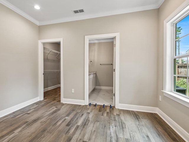 unfurnished bedroom with ensuite bathroom, a walk in closet, hardwood / wood-style flooring, a closet, and ornamental molding