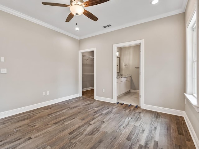 unfurnished bedroom with ensuite bath, a spacious closet, ceiling fan, crown molding, and light wood-type flooring