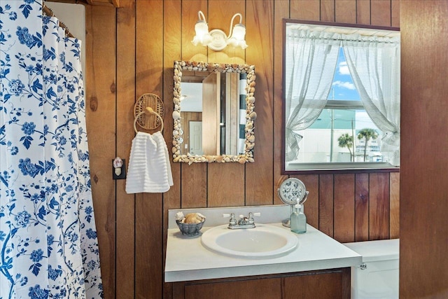 bathroom with vanity, toilet, and wood walls