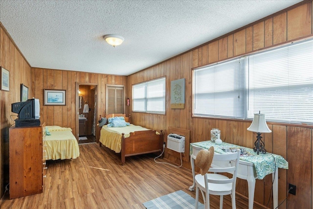 bedroom featuring hardwood / wood-style flooring, a wall mounted air conditioner, a textured ceiling, and wood walls