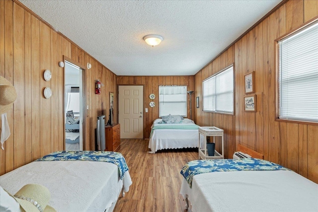 bedroom featuring wood walls, a textured ceiling, and light wood-type flooring