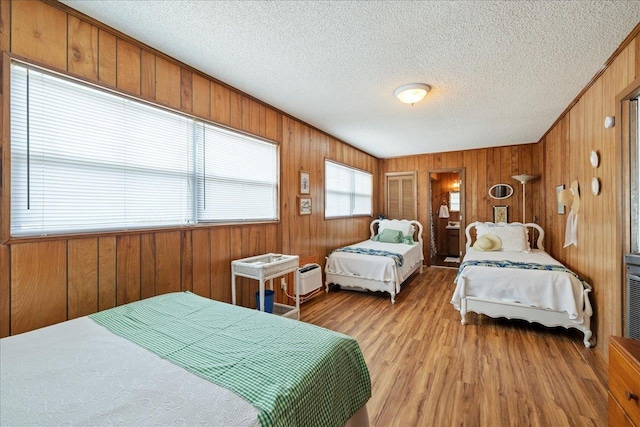 bedroom with light hardwood / wood-style flooring, wooden walls, and a textured ceiling