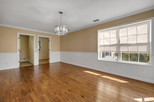 empty room featuring visible vents, wainscoting, ornamental molding, wood finished floors, and a chandelier