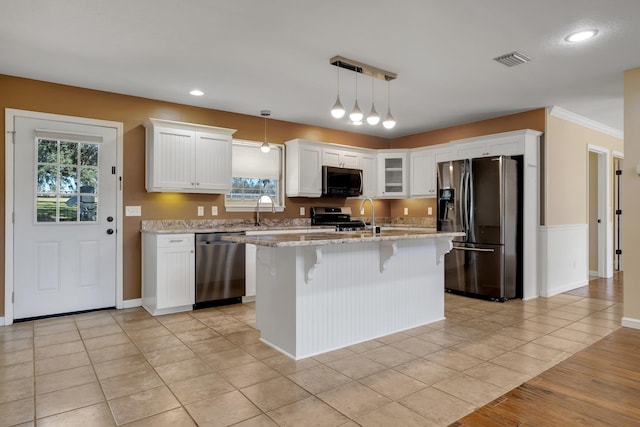 kitchen featuring a center island, pendant lighting, stainless steel appliances, visible vents, and glass insert cabinets