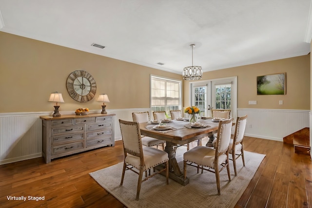 dining area featuring wainscoting, a notable chandelier, visible vents, and wood finished floors