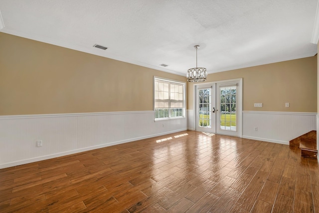 empty room with visible vents, wainscoting, wood finished floors, french doors, and a chandelier