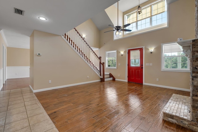 entrance foyer featuring wood finished floors, a towering ceiling, visible vents, a ceiling fan, and stairway