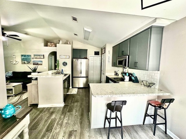 kitchen featuring a kitchen bar, lofted ceiling, kitchen peninsula, dark hardwood / wood-style floors, and appliances with stainless steel finishes