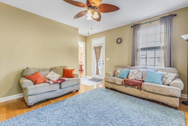 living room featuring ceiling fan, light wood finished floors, and baseboards