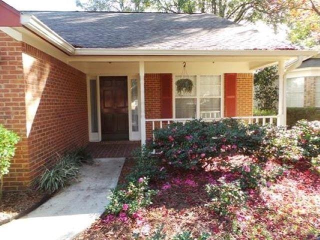 property entrance with a shingled roof, a porch, and brick siding