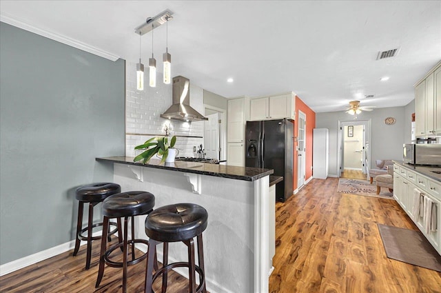 kitchen featuring stainless steel microwave, black fridge, backsplash, a kitchen bar, and wall chimney range hood